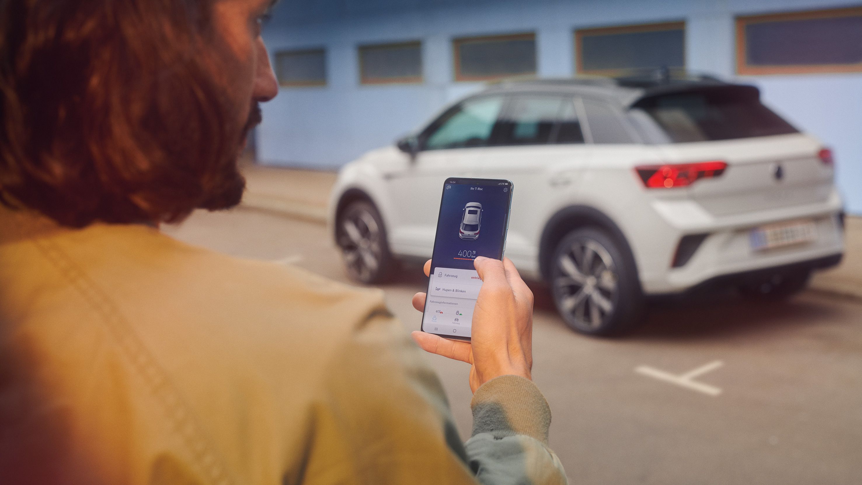 Ein Mann nutzt die Volkswagen App auf seinem Smartphone, im Hintergrund steht ein weißer T-Roc