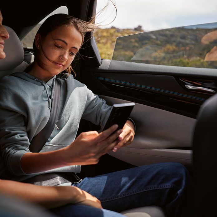 Zwei Frauen sitzen auf Rückbank eines VWs ID.7 und sehen sich am Smartphone einen digitalen Katalog an