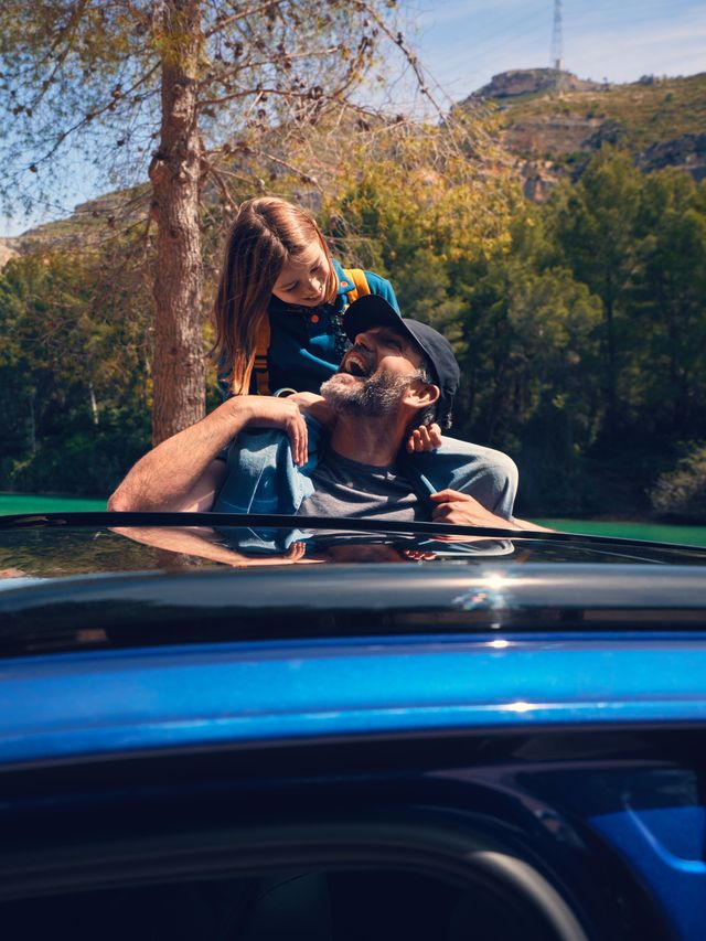 Ein Vater mit seiner Tochter auf den Schultern steht bei einem VW Touareg R eHybrid