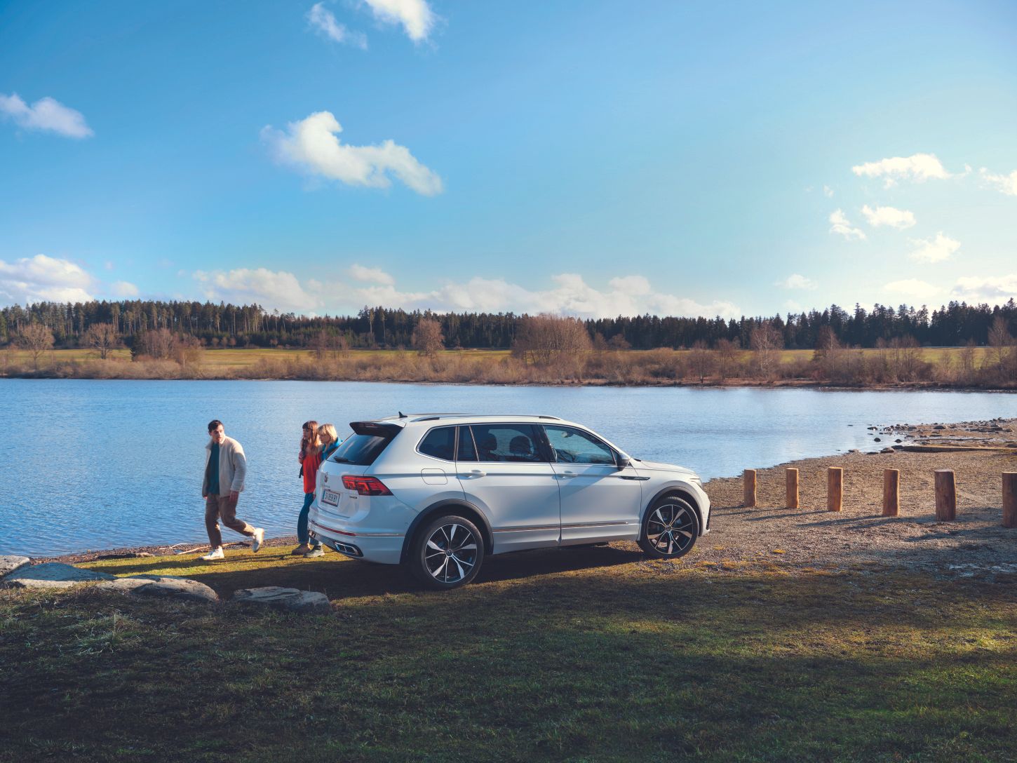 VW Tiguan Allspace steht an einem See, dahinter gehen drei Personen vorbei