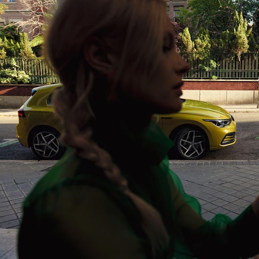 Eine Frau bedient ihr Smartphone, hinter ihr parkt ein VW Golf.