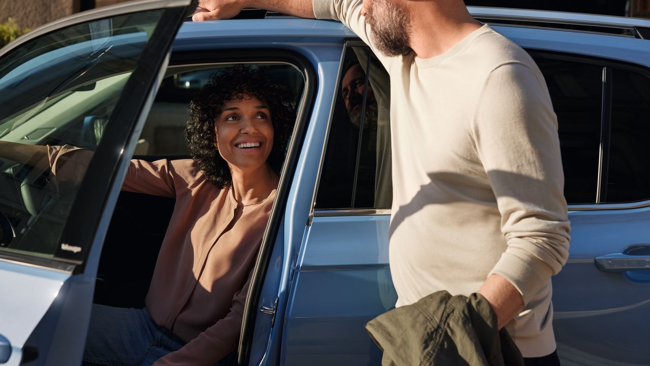 Mann redet mit einer Frau, die am Fahrersitz eines blauen VW T-Cross sitzt