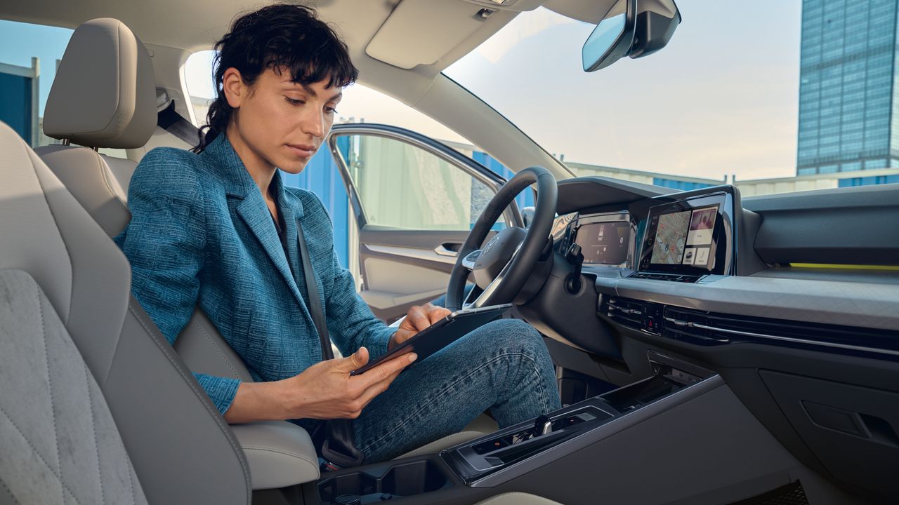 Eine Frau sitzt auf dem Fahrersitz eines geparkten VW golf 8 und schaut auf ein Tablet