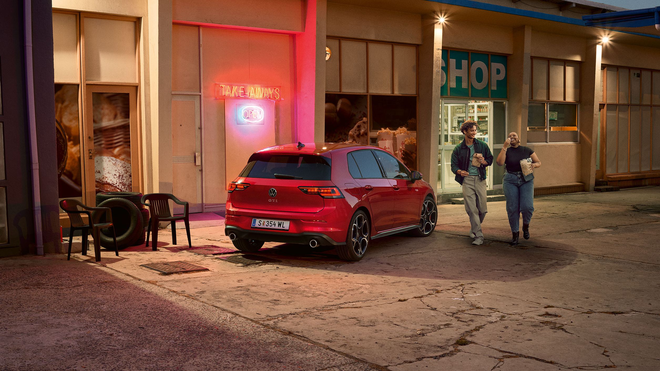 Heckansicht eines roten VW Golf GTI in abendlicher Stimmung, zwei Personen gehen neben ihm her