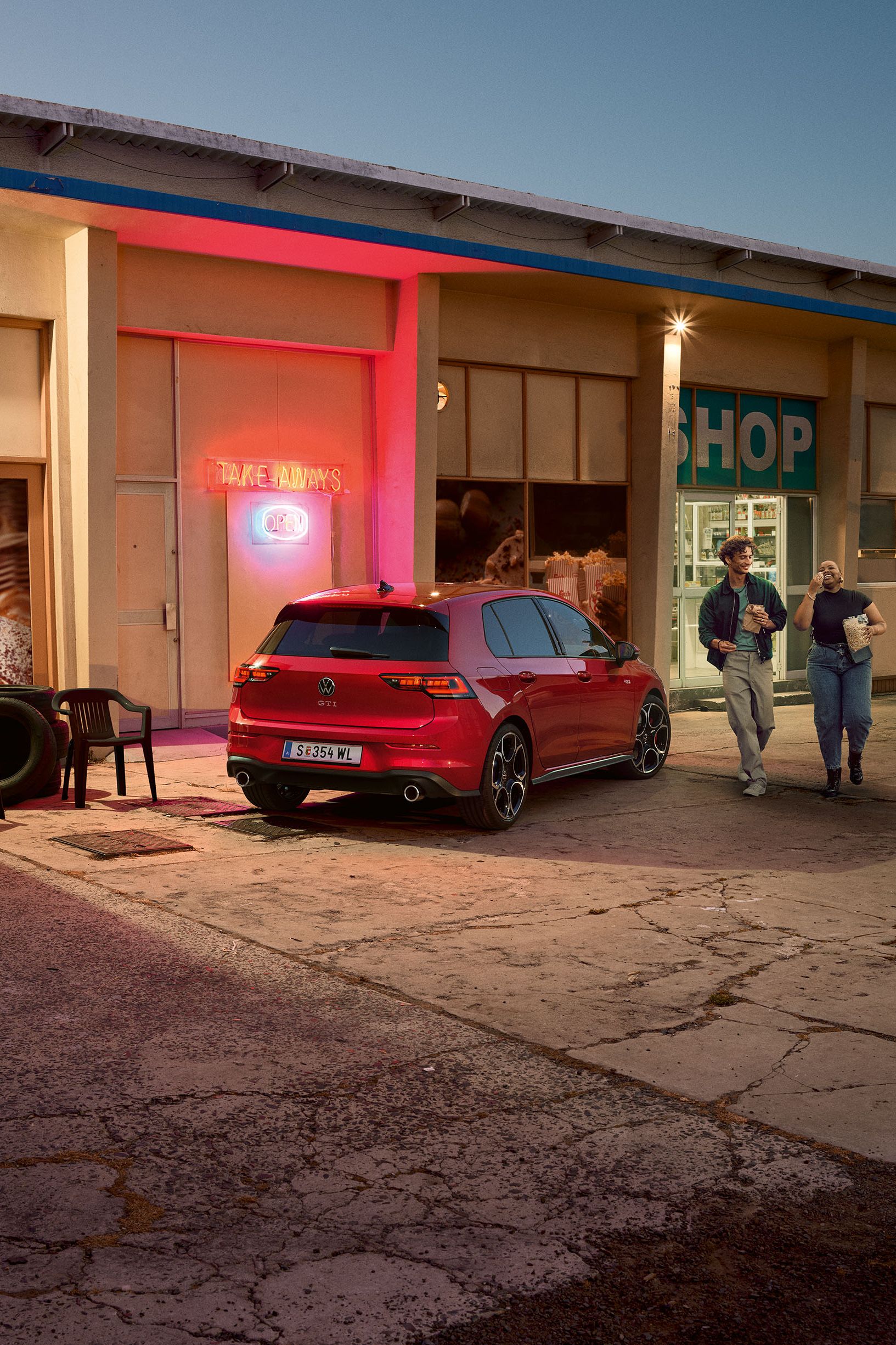 Heckansicht eines roten VW Golf GTI in abendlicher Stimmung, zwei Personen gehen neben ihm her