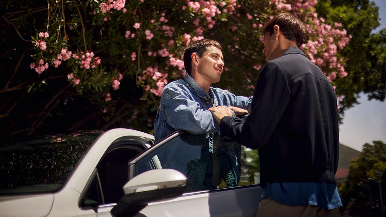 Zwei Männer stehen an der Tür eines weißen VW Golf und schauen sich gegenseitig an