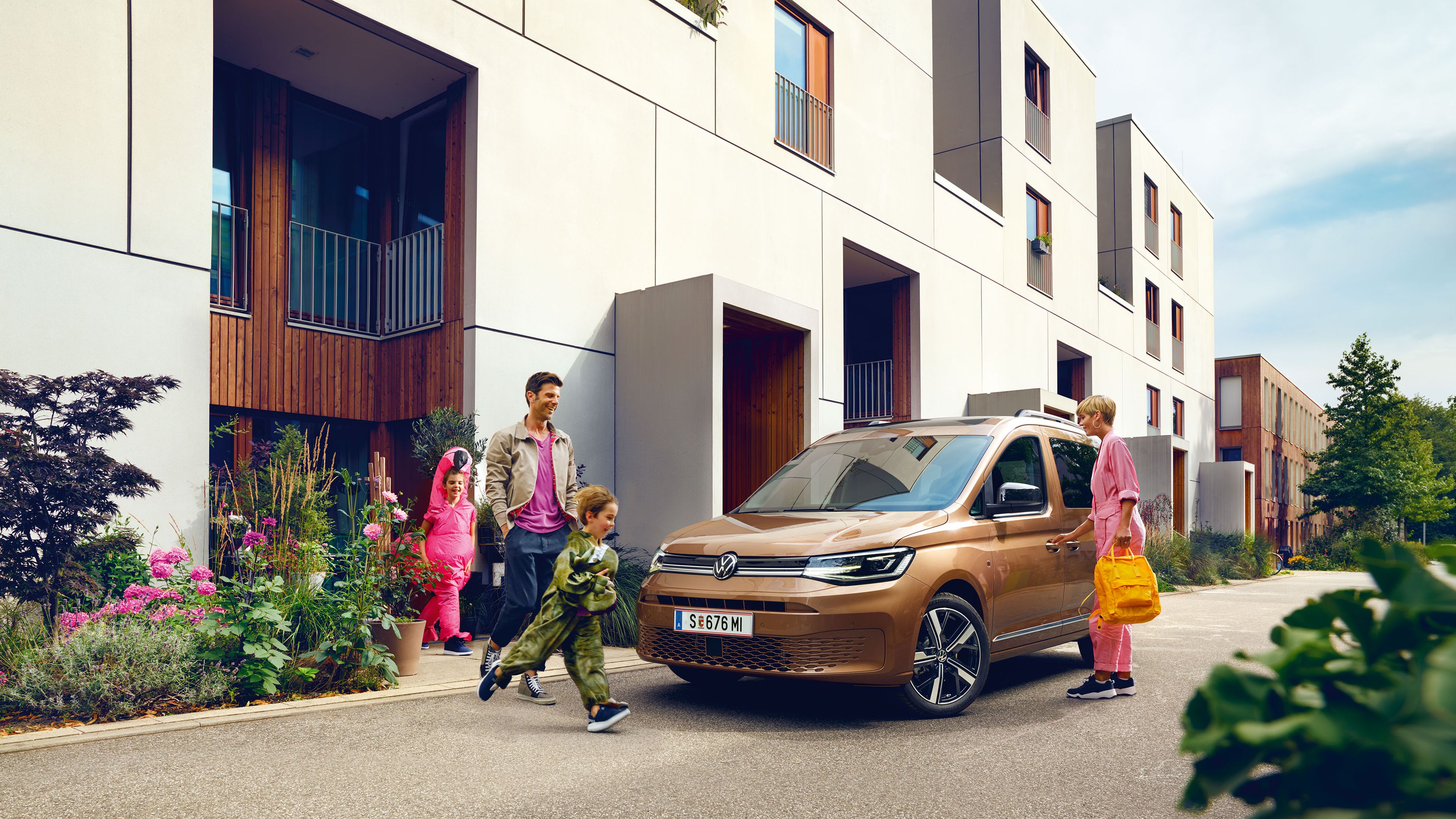 Eine junge Familie steigt vor der Wohnung in einen VW Caddy ein.