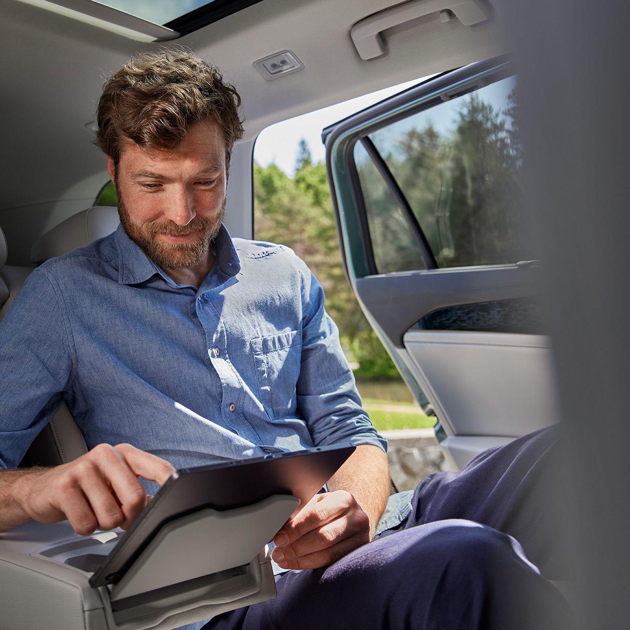 Ein Mann sitzt auf der Rücksitzbank eines VW Passat und bedient ein Tablet in der Mittelkonsole
