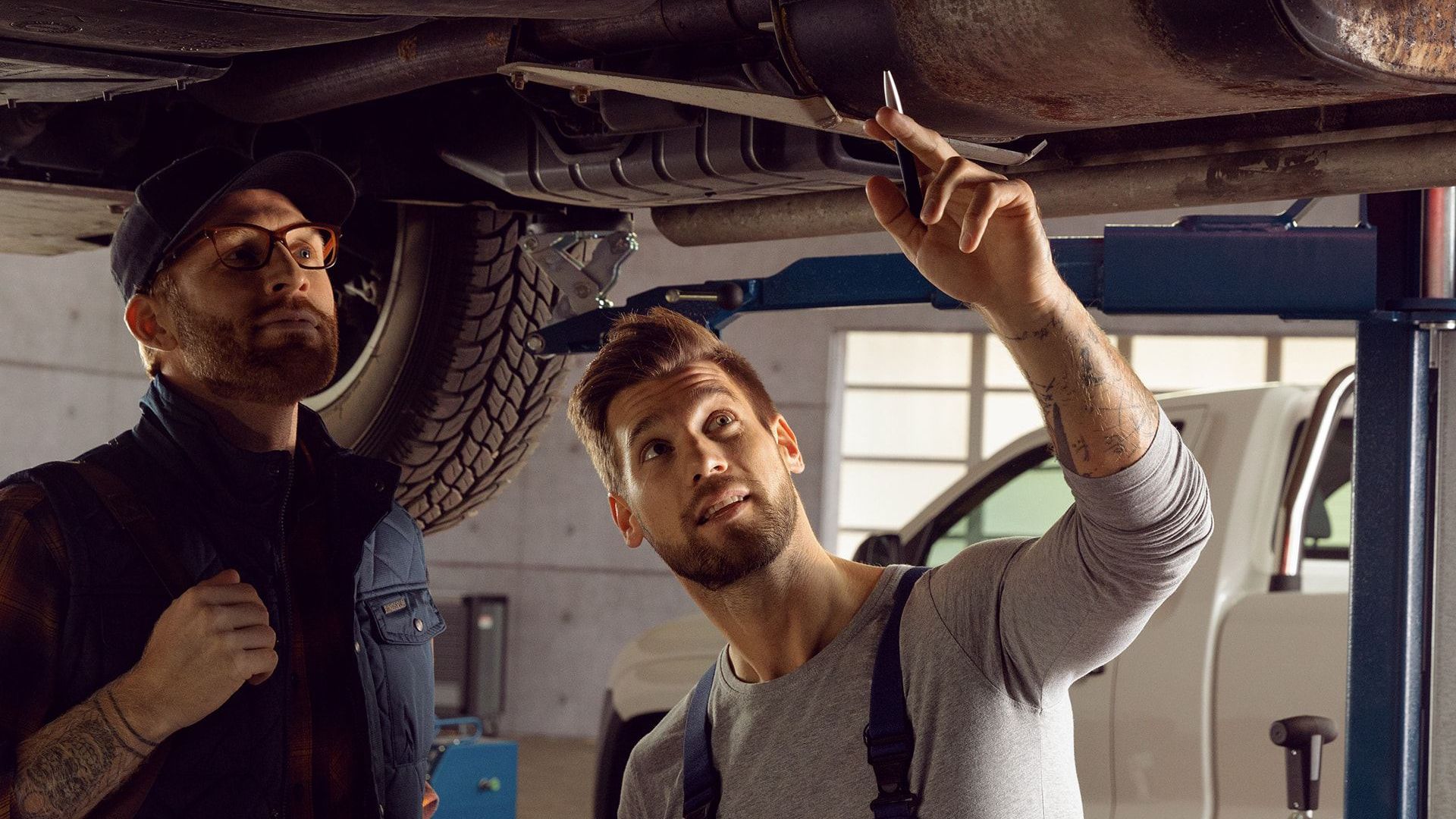 Zwei Männer stehen unter Fahrzeug in VW Service Werkstatt.