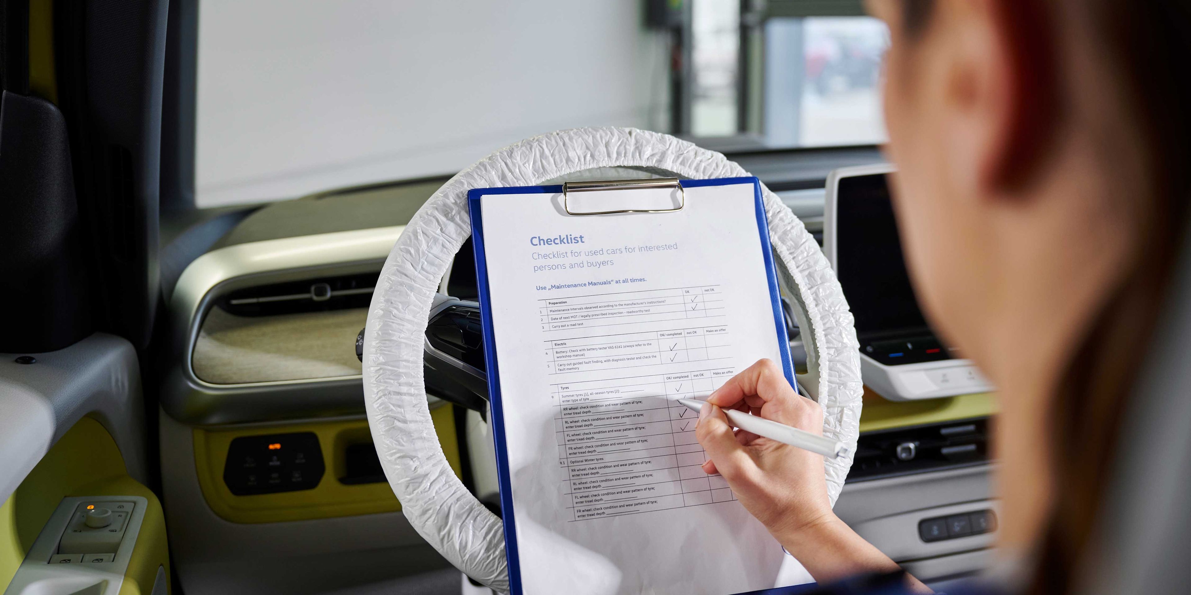 Eine Volkswagen Service Technikerin hakt die Checkpunkte auf einer Liste ab