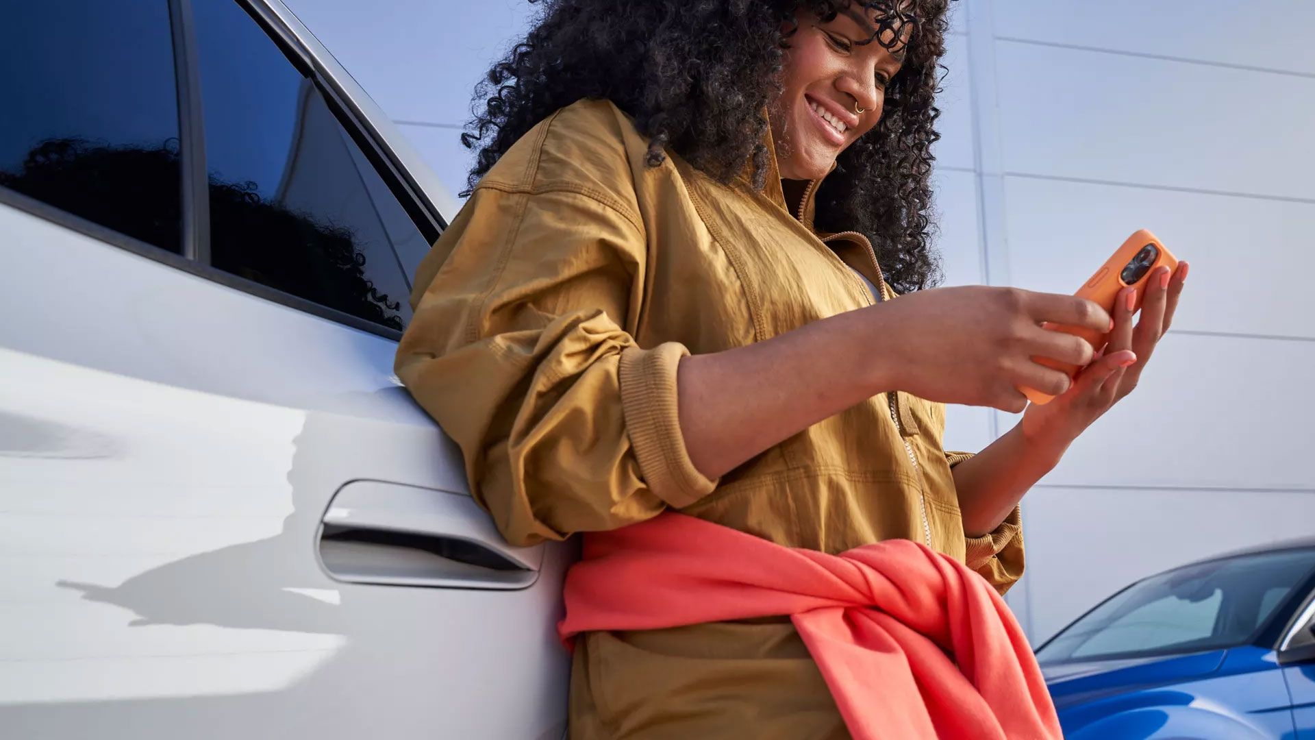 Eine Frau lehnt an einem VW ID. und blickt auf ihr Smartphone