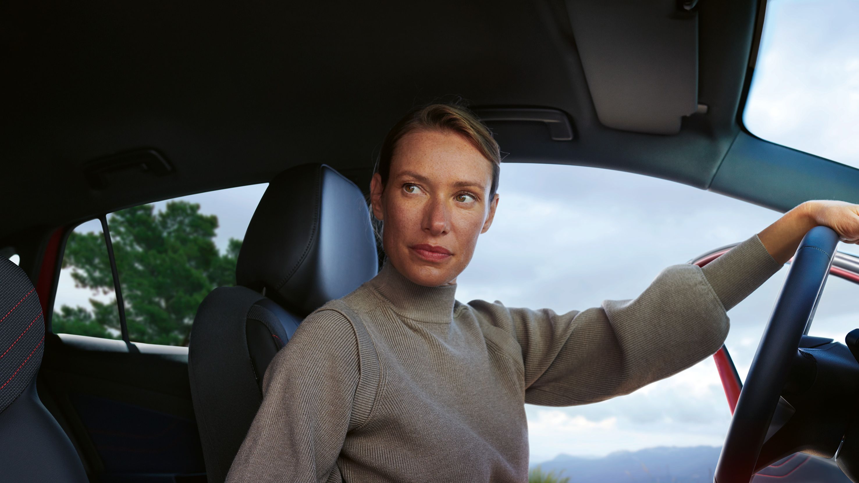Eine Frau sitzt auf dem Fahrersitz in einem roten VW ID.5 GTX. Im Hintergrund ein Bergpanorama.