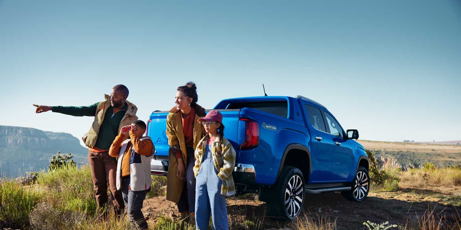 Eine Familie parkt mit einem blauen Amarok in den Bergen und blickt in die Ferne