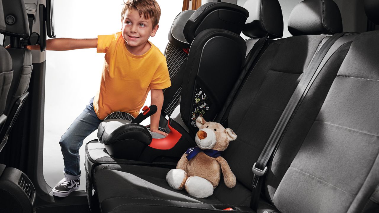 Kind steigt in einen VW Caddy ein und will sich in den Kindersitz setzen