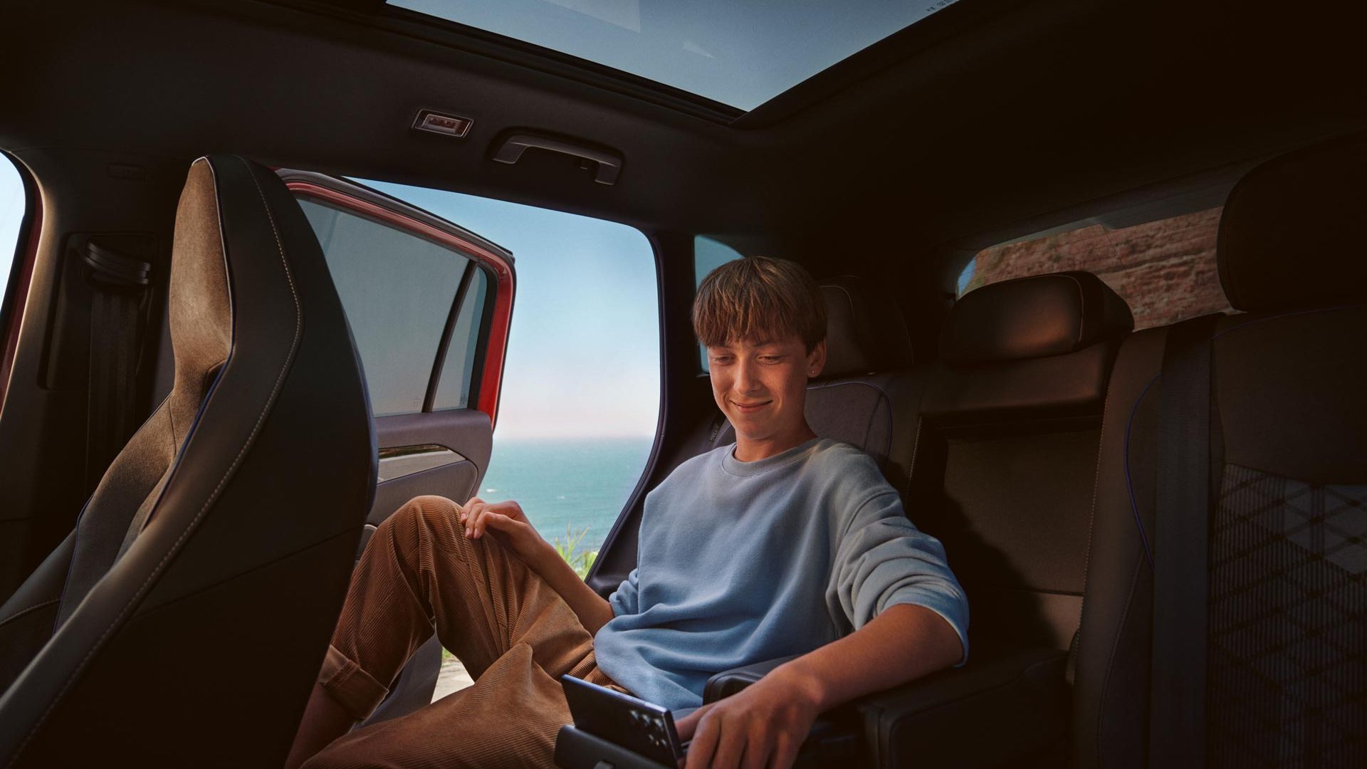 Jugendlicher sitzt auf Rückbank im VW Tiguan und bedient Smartphone in Halterung