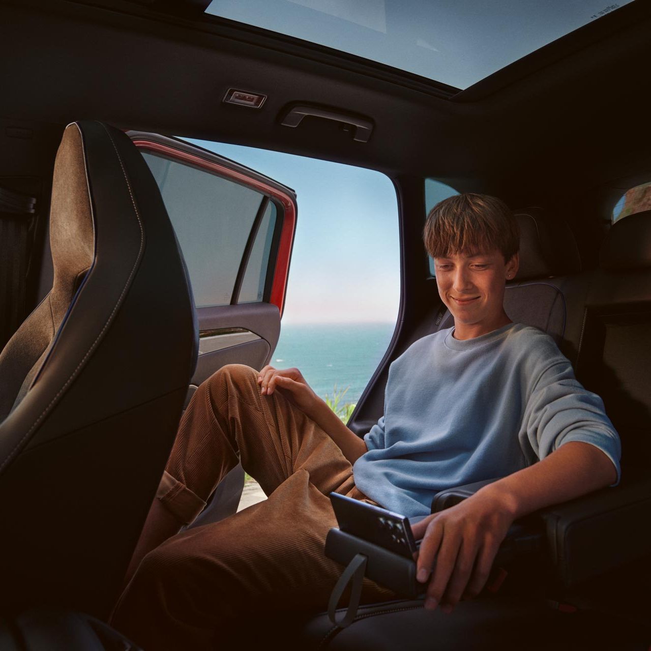 Jugendlicher sitzt auf Rückbank im VW Tiguan und bedient Smartphone in Halterung