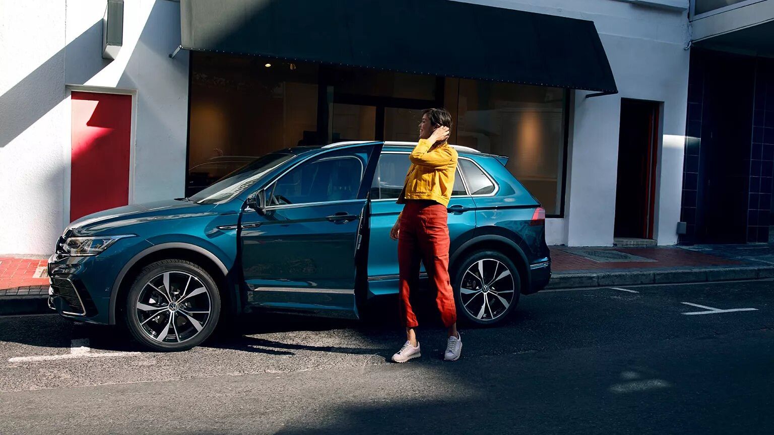VW Tiguan in blau parkt vor Gebäude. Frau steht davor.