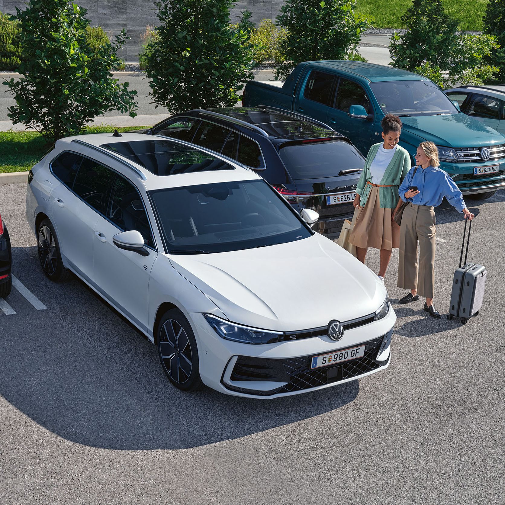 Zwei Frauen stehen neben einem weißen VW Passat R-Line auf einem Parkplatz