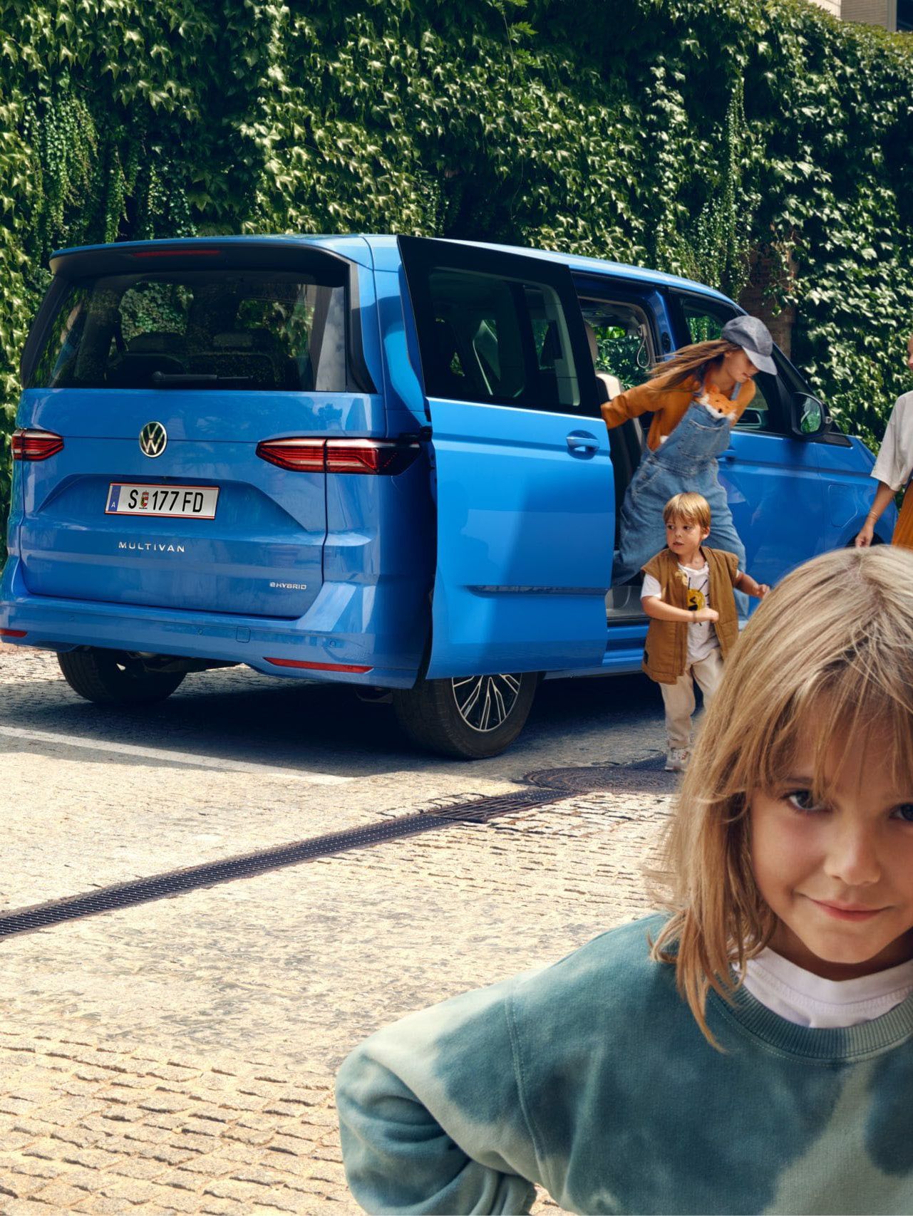 Ein Mädchen steht vor dem neuen VW Multivan T7 2021 und schaut trotzig in die Kamera.