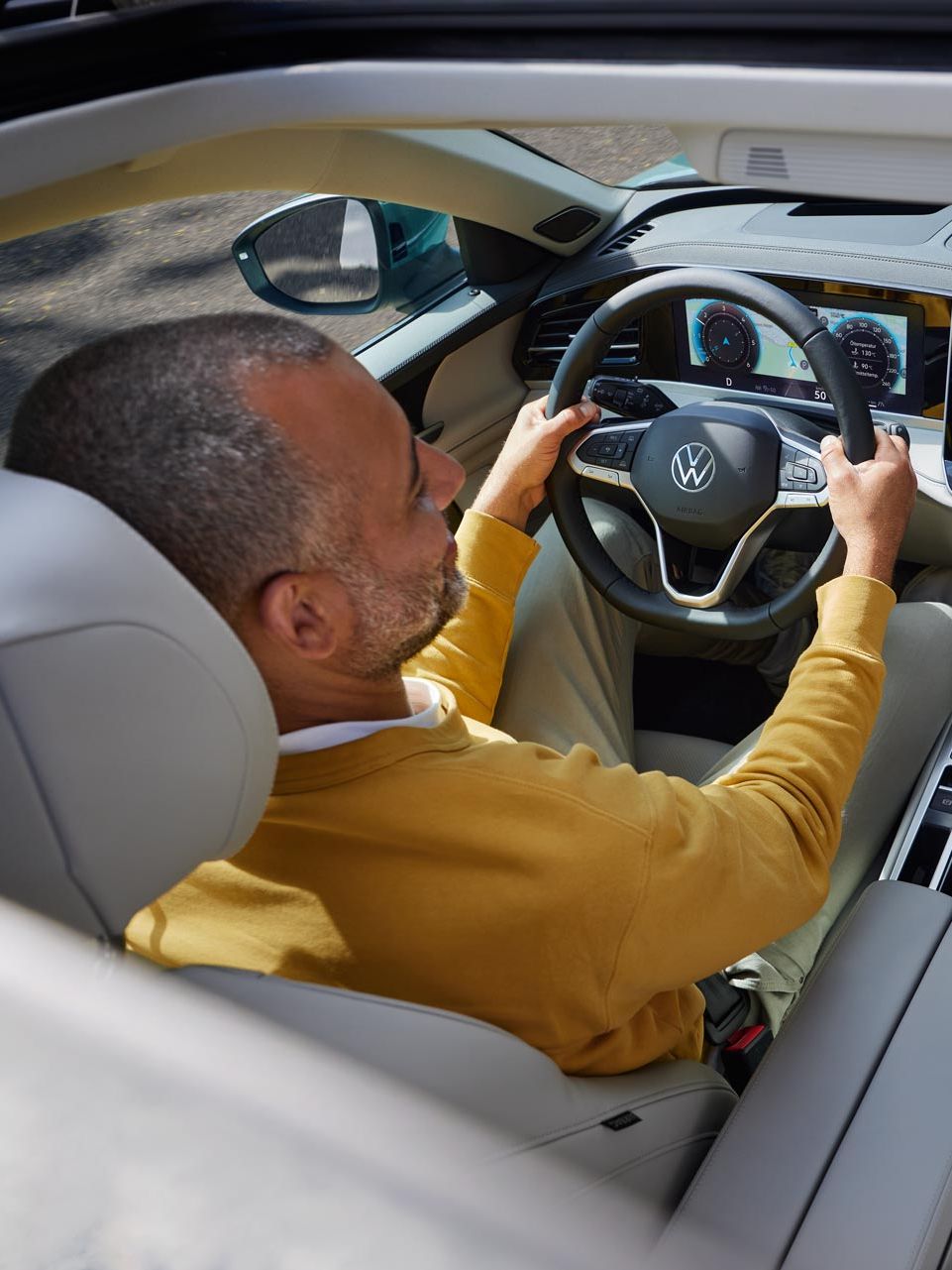 Blick von oben durch das geöffnete optionale Schiebedach des VW Passat, wo ein Mann mit beiden Händen am Lenkrad sitzt.