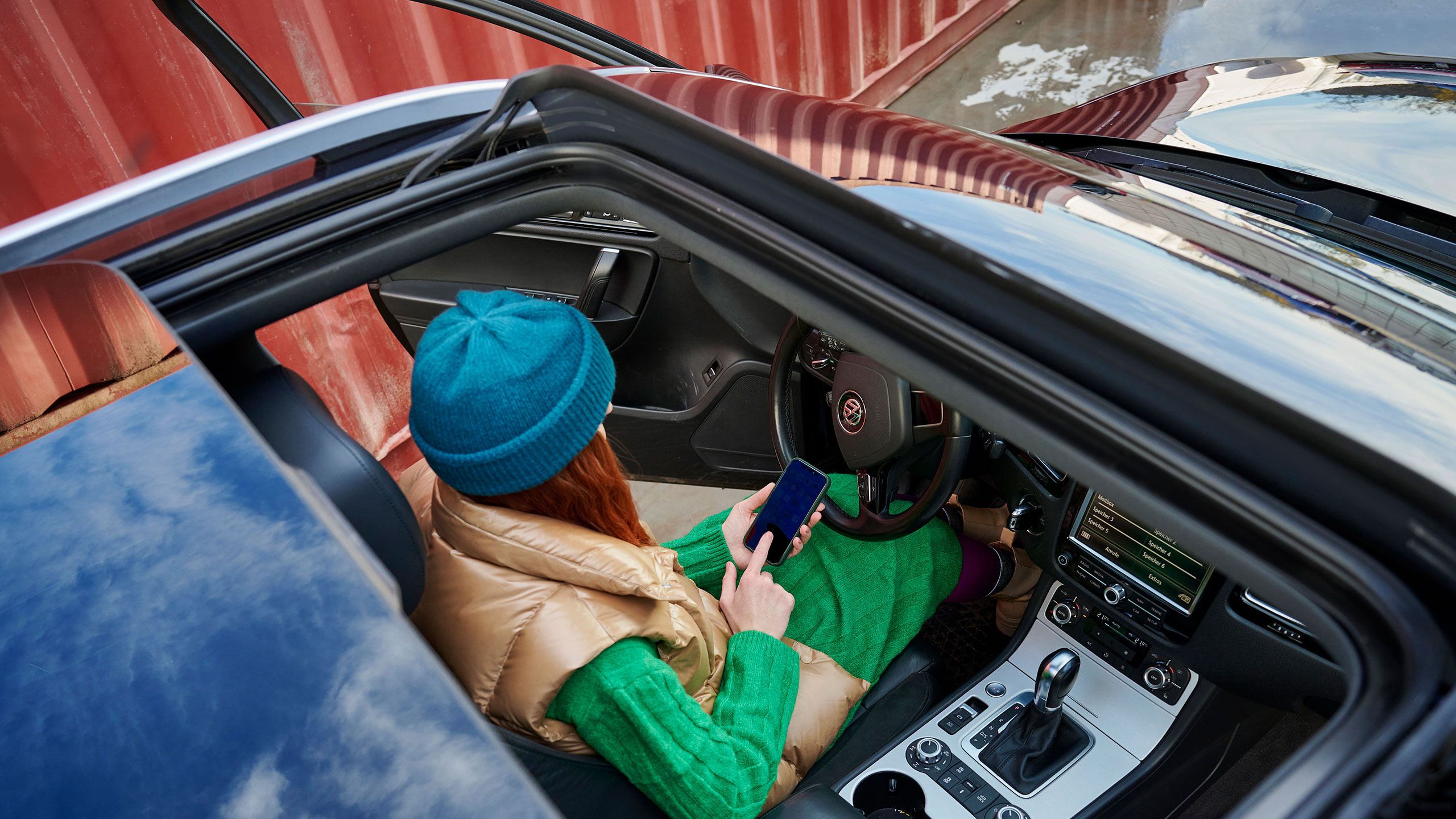 Blick von Panoramadach in ein VW Touareg Vorgängermodell mit Car-Net, Frau bedient Smartphone