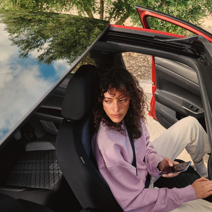 VW Taigo: Blick durchs optionale Panorama-Ausstell/-Schiebedach, Frau sitzt am Fahrersitz