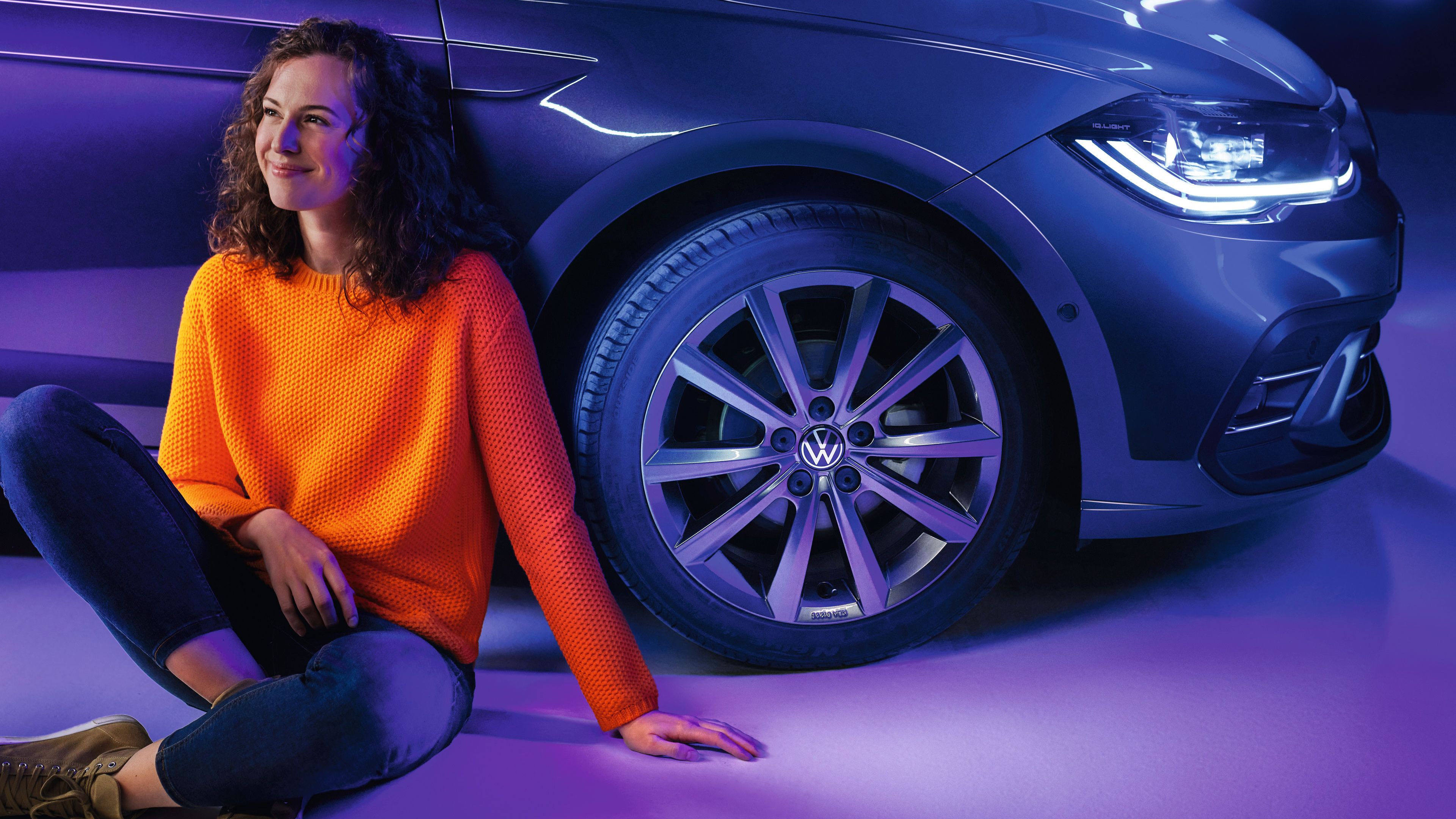Eine Frau sitzt vor ihrem Volkswagen Polo am Boden