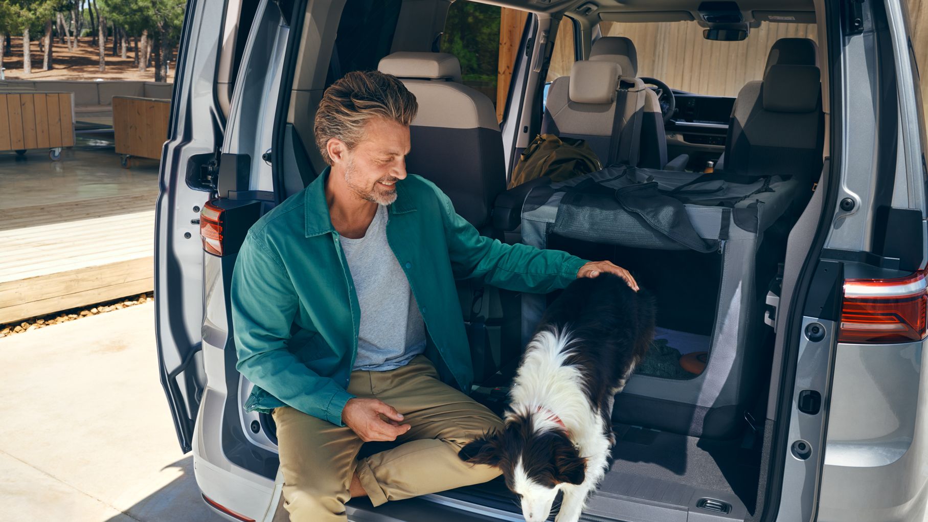 Ein Mann sitzt mit einem Hund im Kofferraum des neuen VW Multivan Life T7 2021.