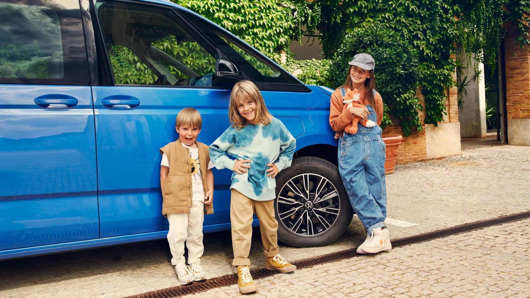 Ein Mädchen und ein Junge stehen vor dem Außenspiegel eines neuen VW Multivan T7 2021.