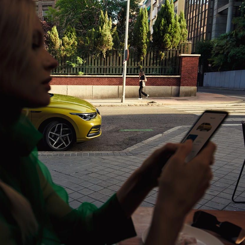 Eine Frau bedient ihr Smartphone, hinter ihr parkt ein VW Golf.