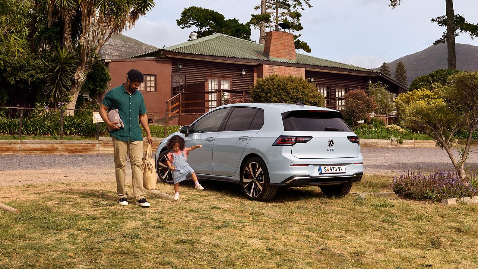 Der neue VW Golf GTE steht auf einem Parkplatz in der Wiese, Vater und Tochter stehen daneben