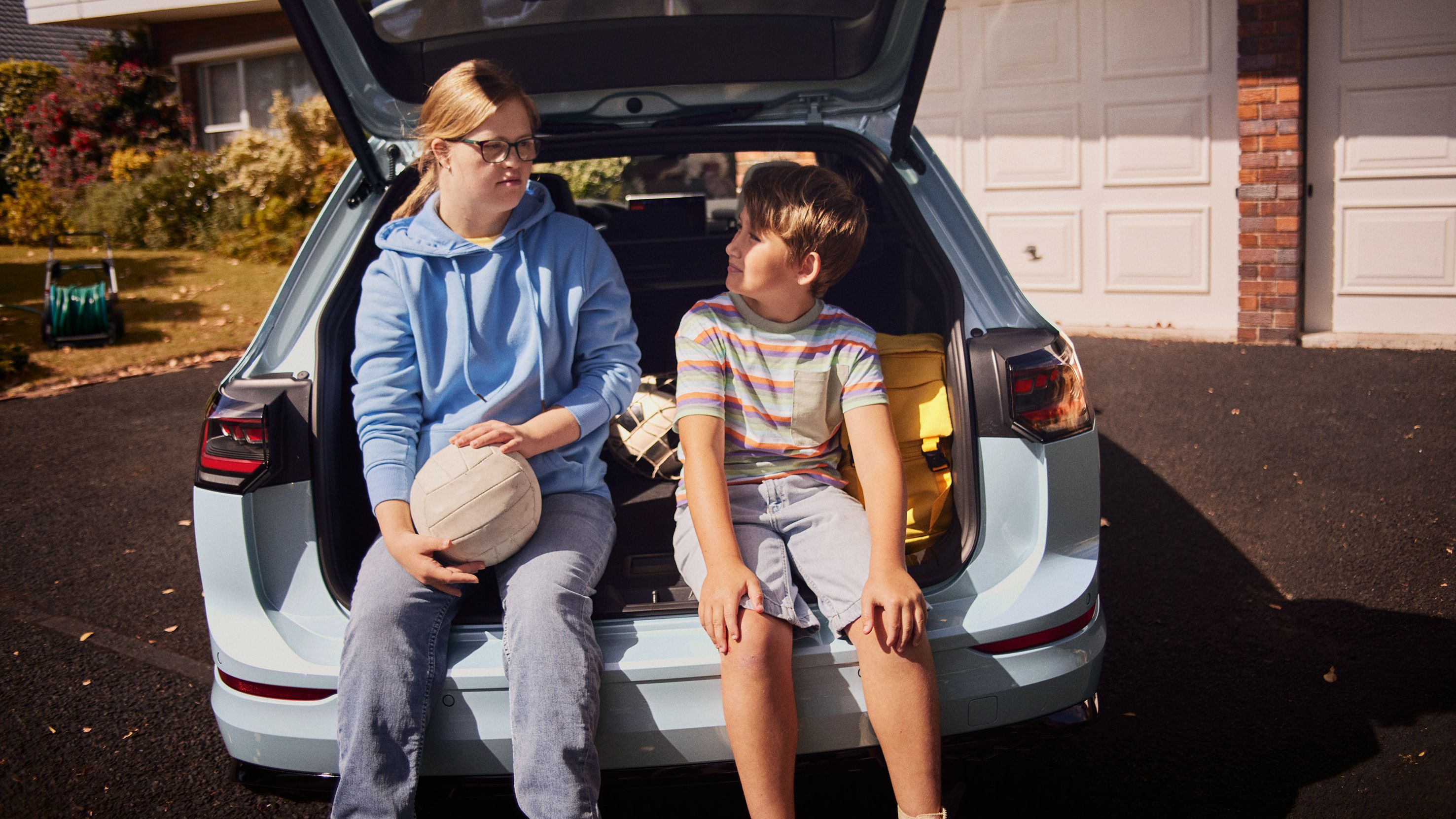 Junge und Mädchen sitzen im Kofferraum des VW Golf Variant