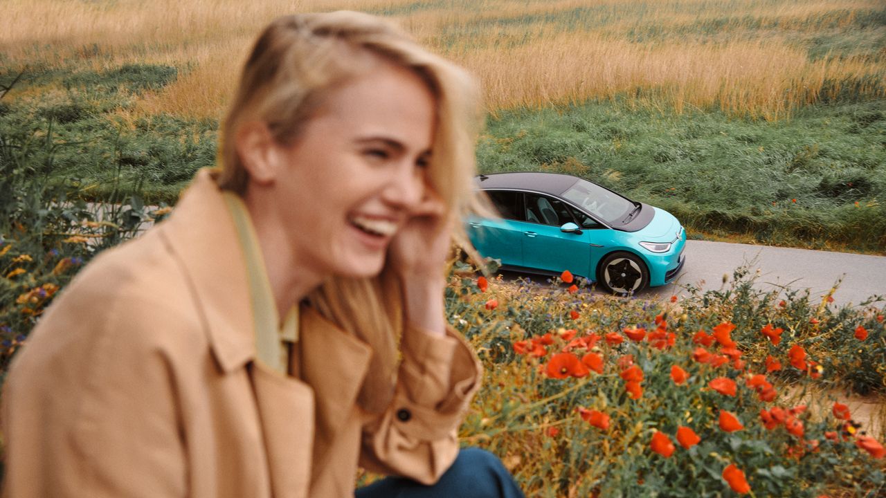 Lächelnde Frau, im Hintergrund sieht man türkisen VW ID.3