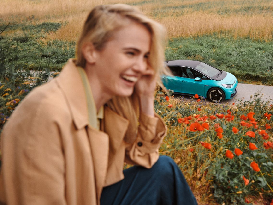 Lächelnde Frau, im Hintergrund sieht man türkisen VW ID.3