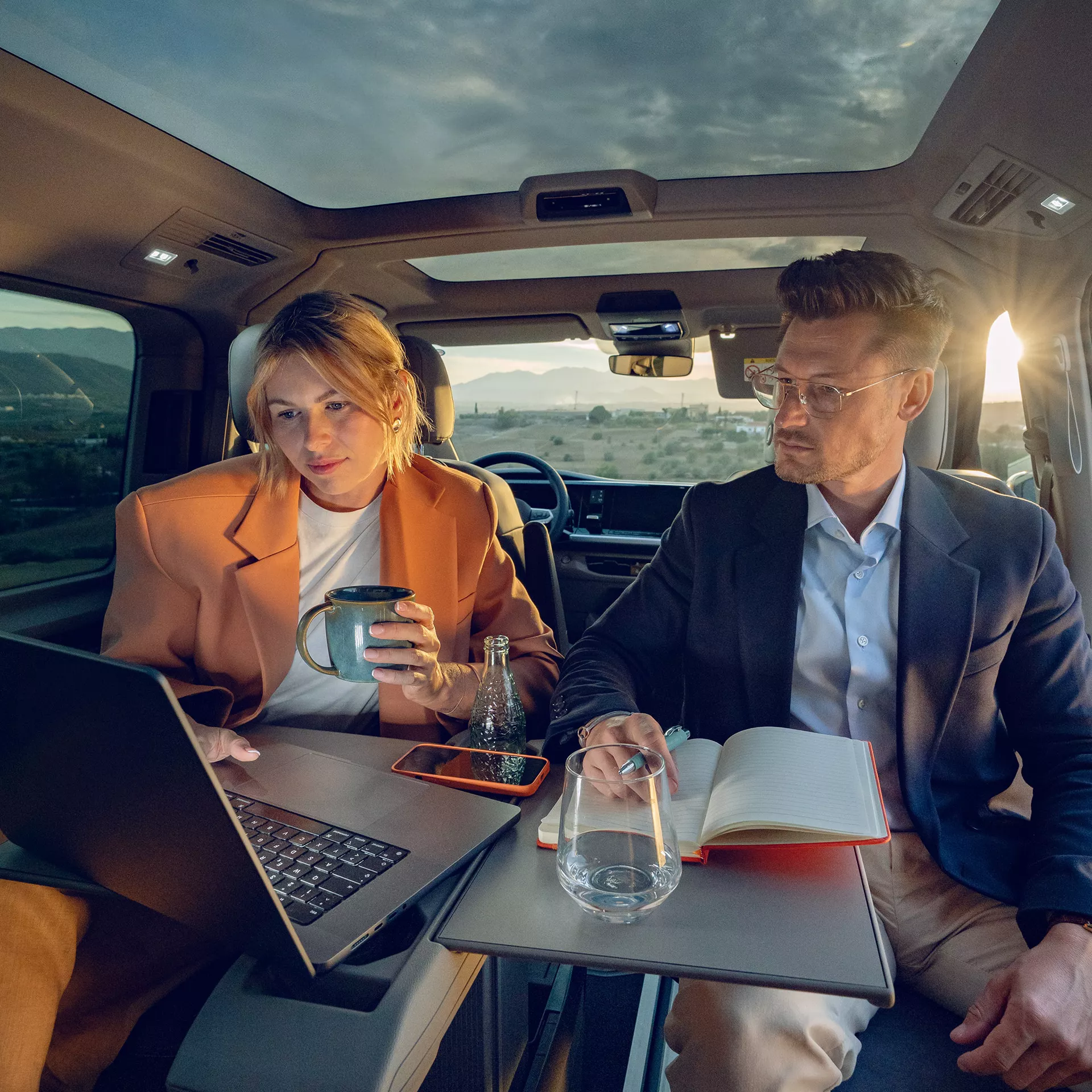 Mann und Frau sitzen im Fond eines neuen VW Multivans, ausgeklappter Tisch, schauen auf Laptop