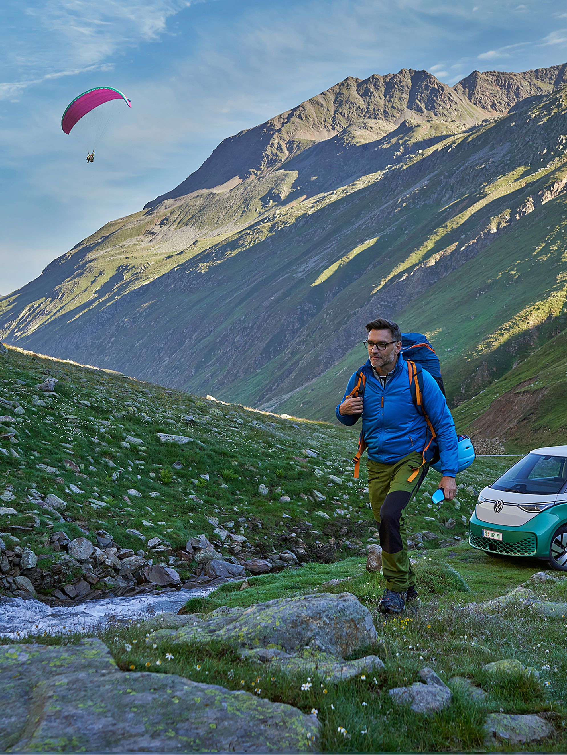 Zwei Wanderer gehen auf einen Berg mit grün weißem ID. Buzz und Paragleiter im Hintergrund