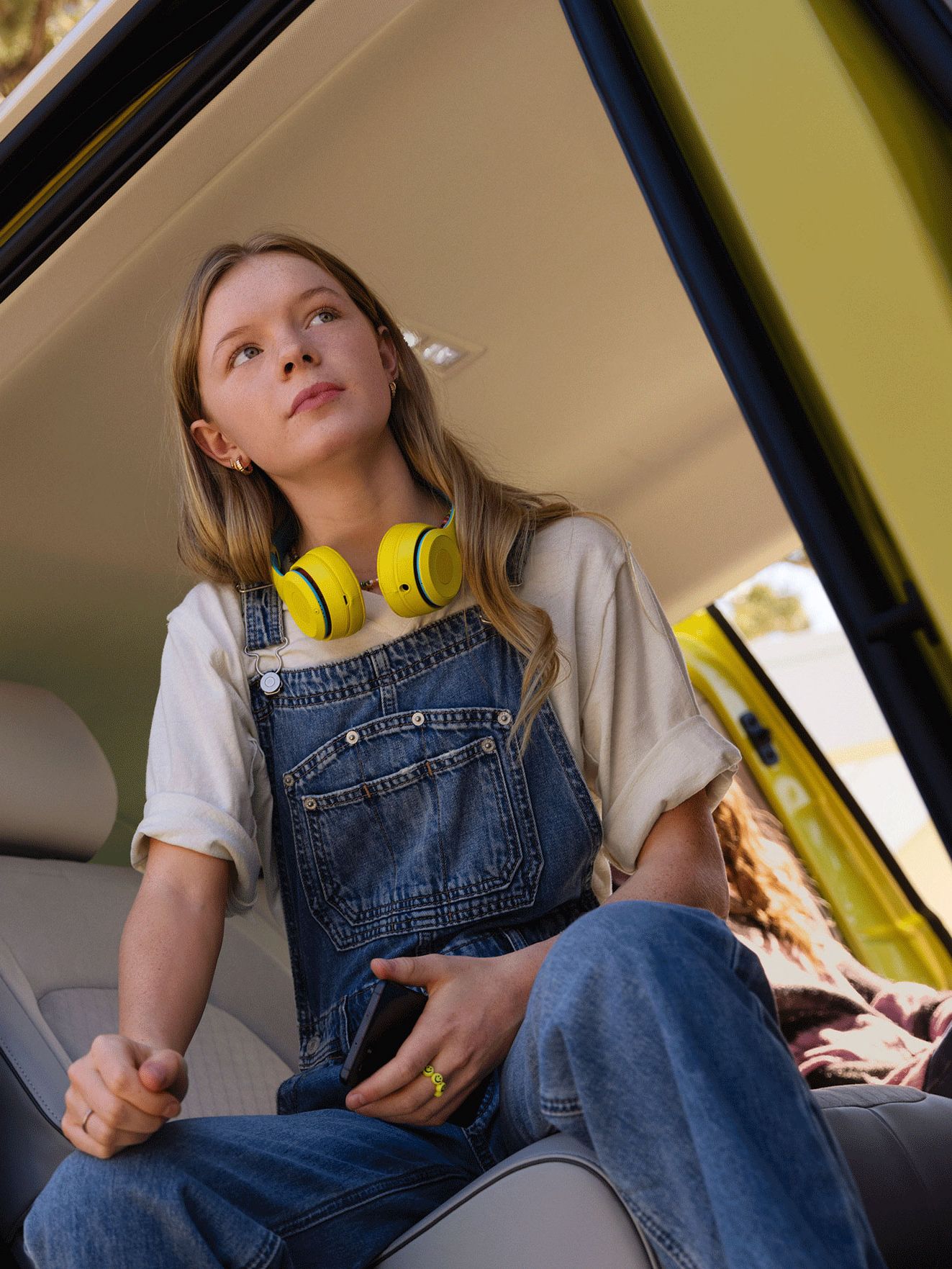 Ein Mädchen mit gelben Kopfhörern sitzt in der Seitentür des VW ID. Buzz.