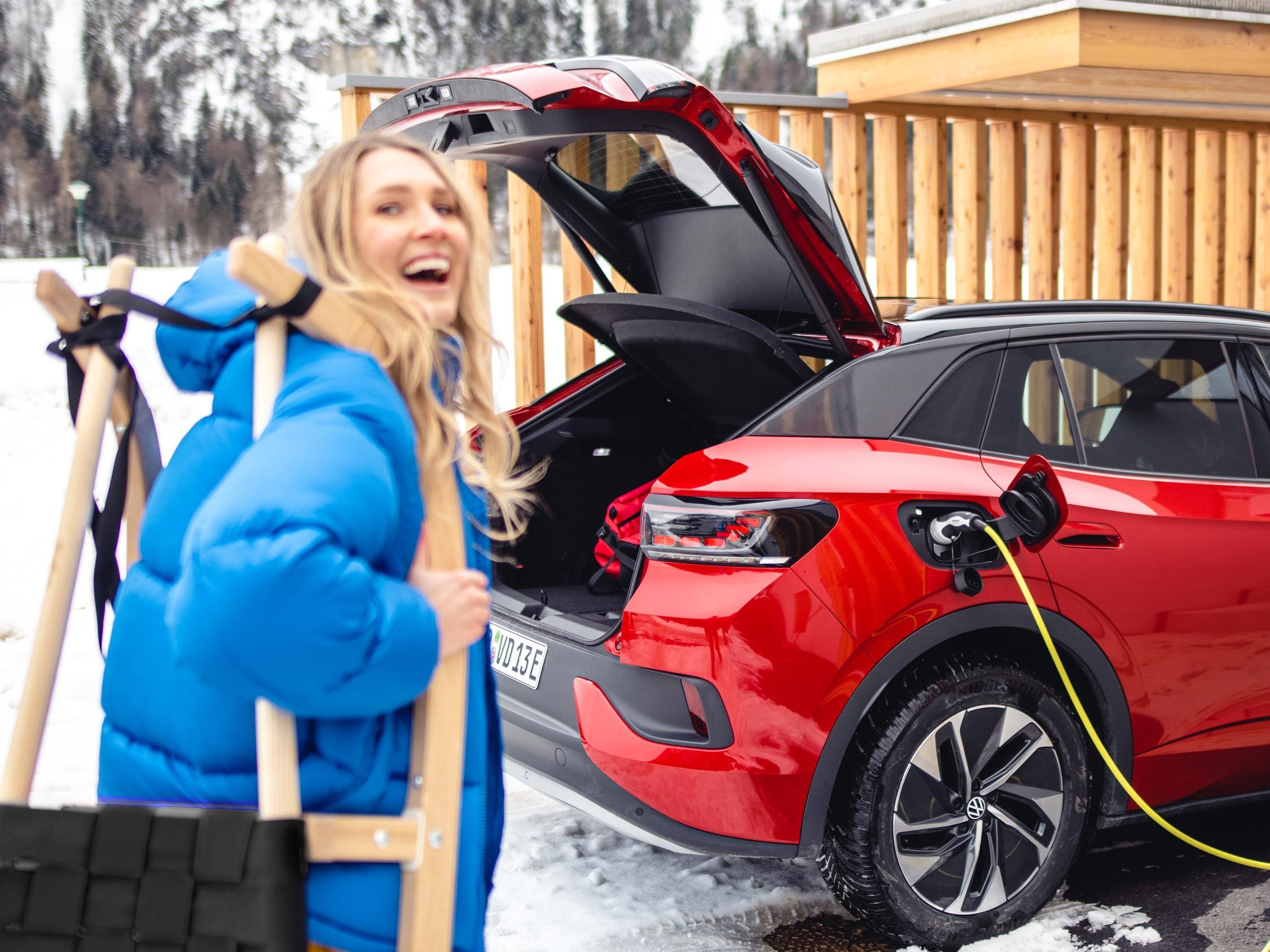 Eine Frau steht lachend vor einem roten Volkswagen im Schnee