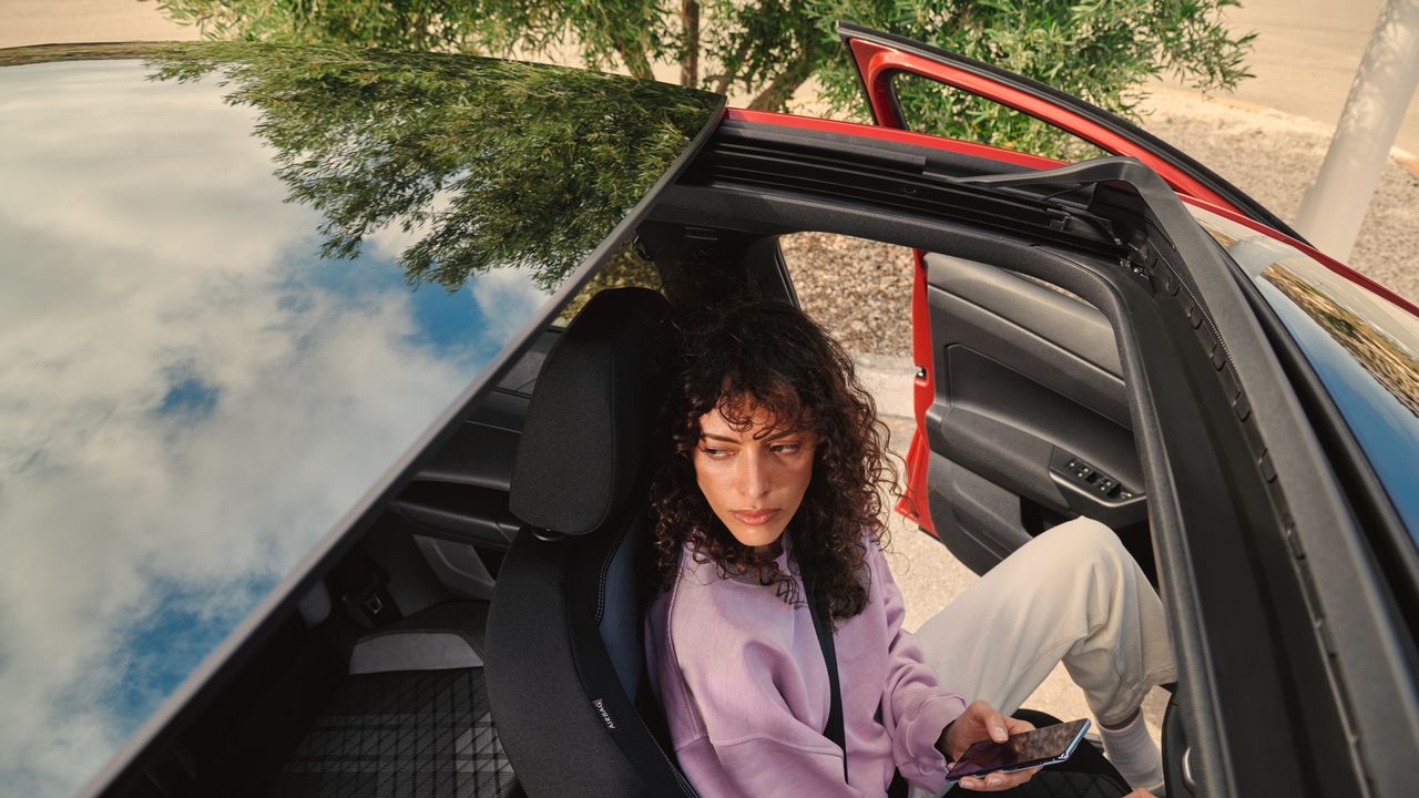 VW Taigo: Blick durchs optionale Panorama-Ausstell/-Schiebedach auf Frau im Fahrersitz