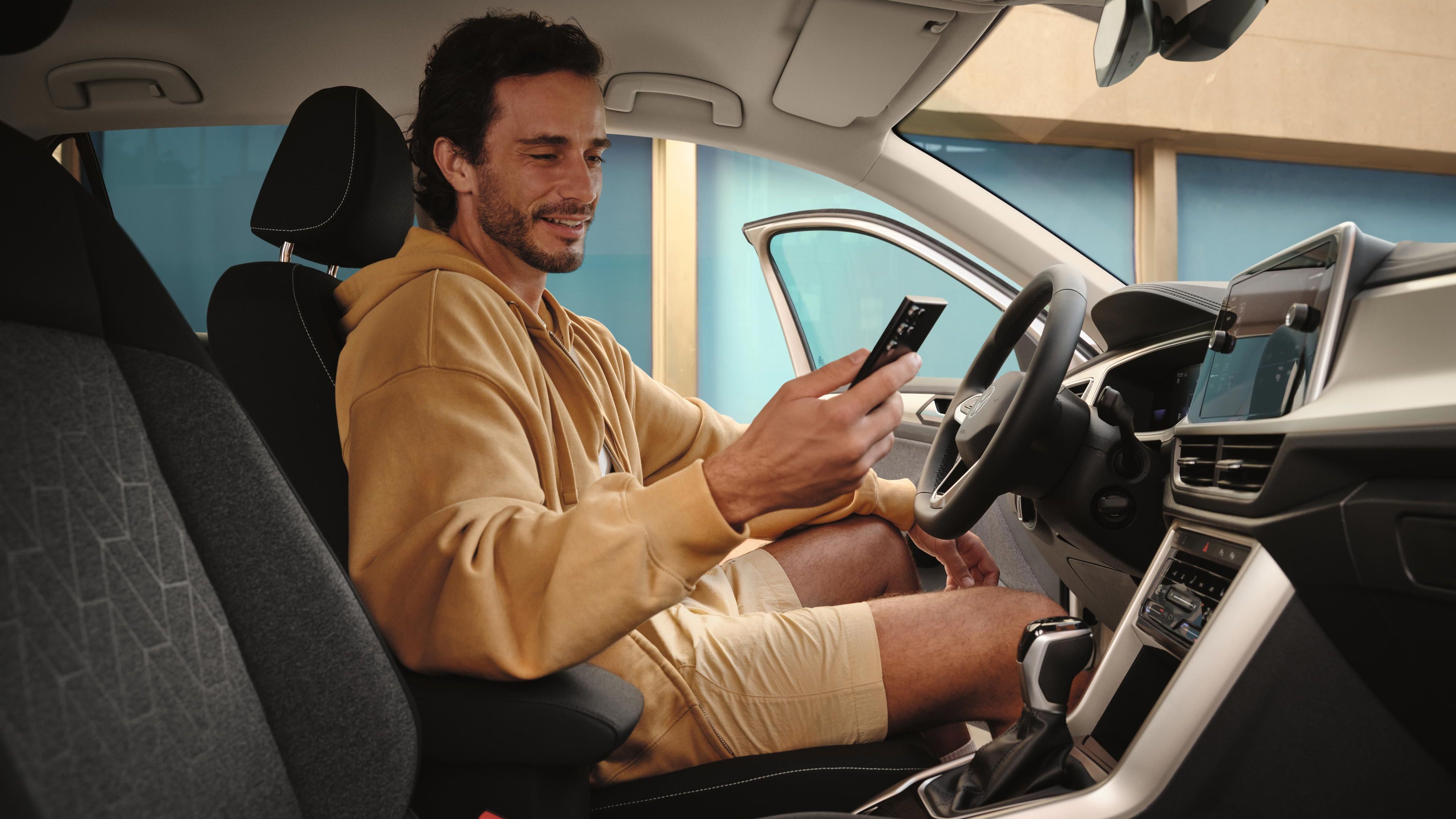 Ein Mann sitzt in einem geparkten VW T-Roc und schaut auf sein Handy