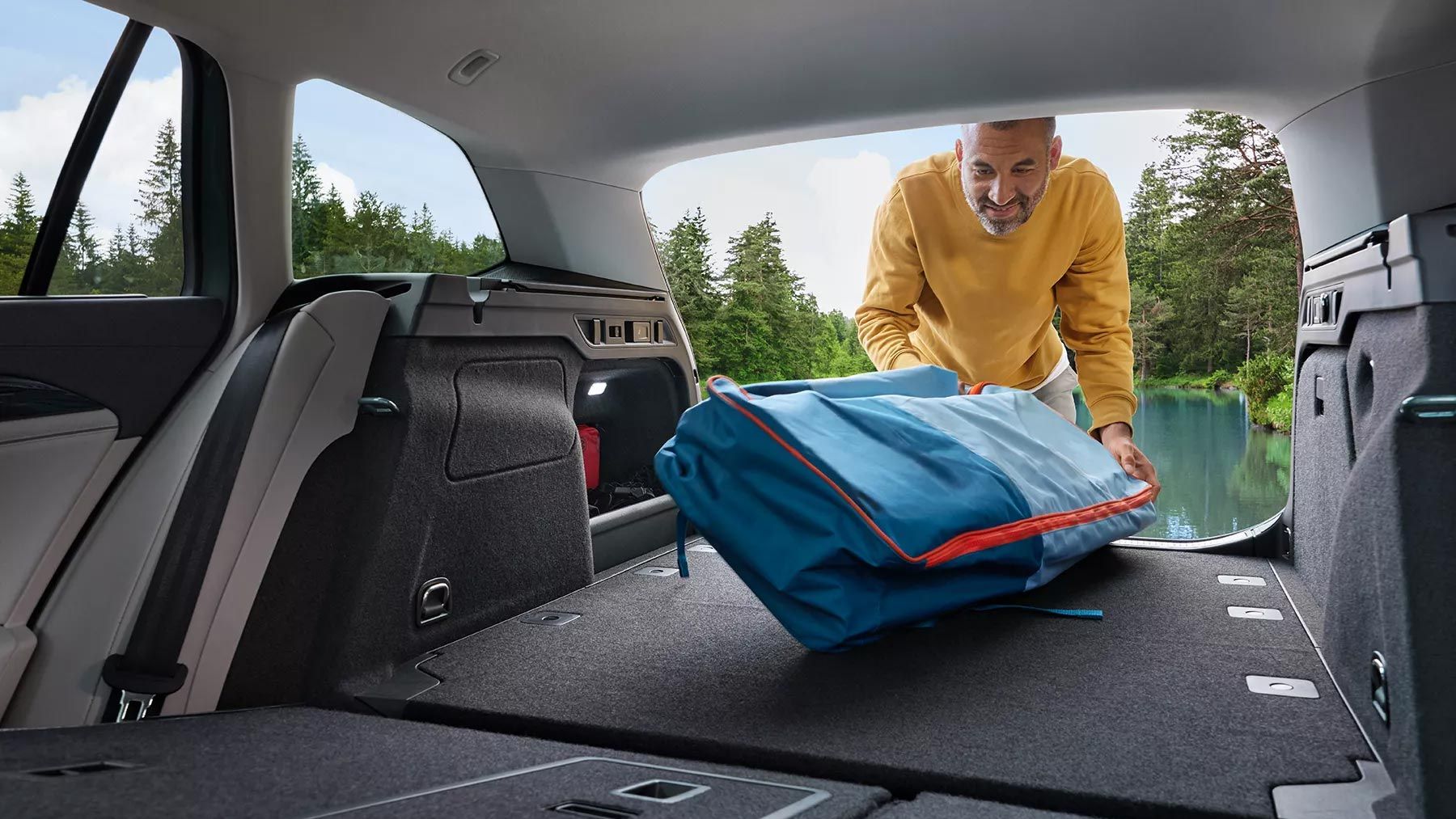 Mann legt großen Rucksack in den geräumigen Kofferraum des VW Passat