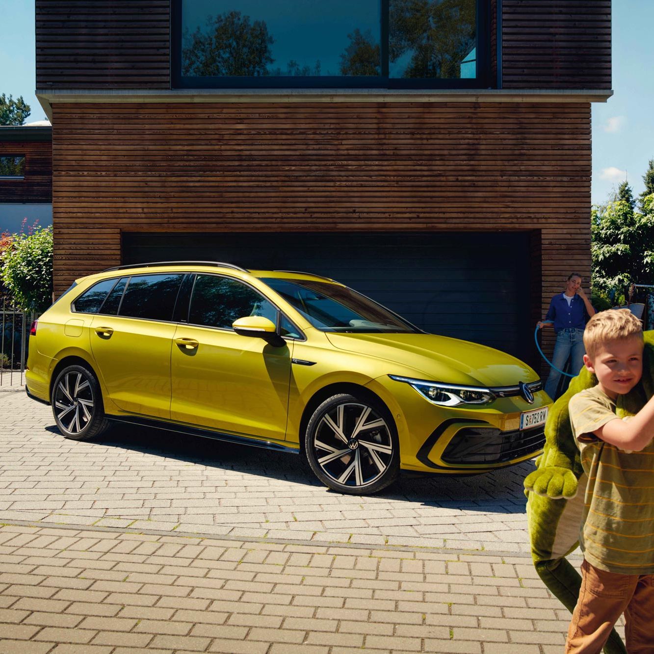 Junge mit Stoff-Krokodil steht vor gelbem VW Golf Variant