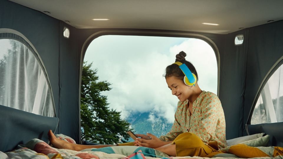 Ein Mädchen hört Musik in einem Bett im VW California 6.1