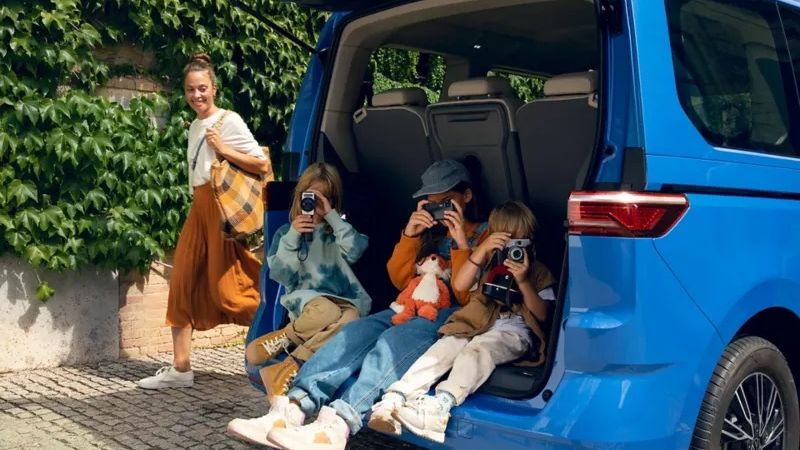 VW-Multivan mit geöffneter Heckklappe-drei Kinder sitzen in der Öffnung