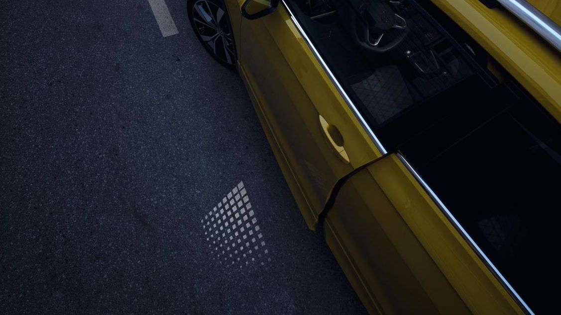Die nur einen Spalt geöffnete VW T-Cross Fahrertür von oben, mit sichtbarer Lichtprojektion in der Dämmerung.
