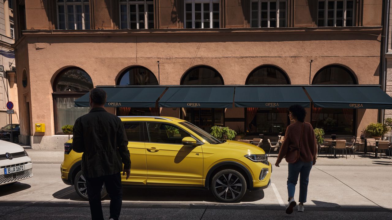 Mann und Frau nähern sich einem gelben VW T-Cross am Straßenrand.