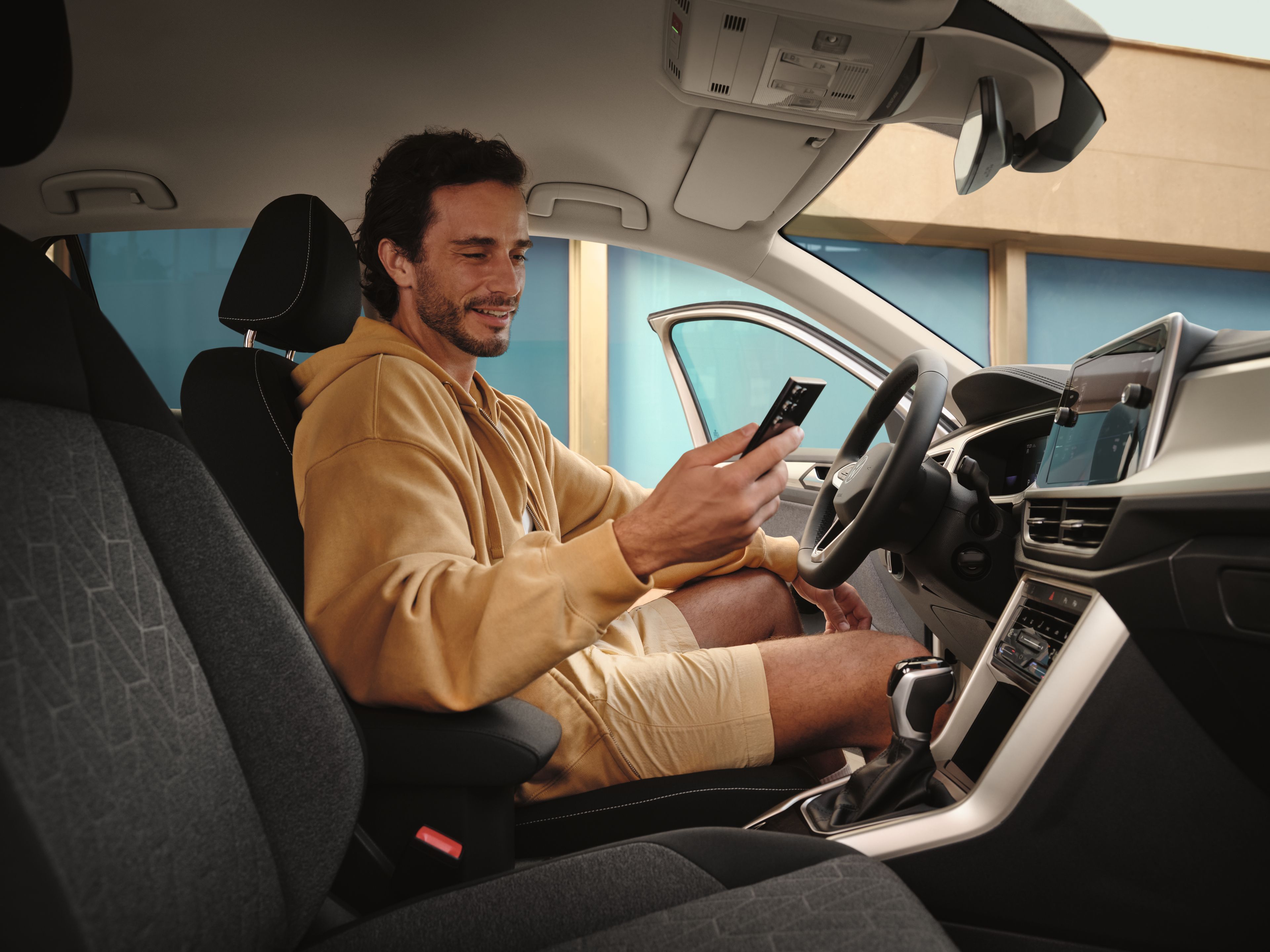 Mann sitzt in VW T-Roc und blickt auf Smartphone