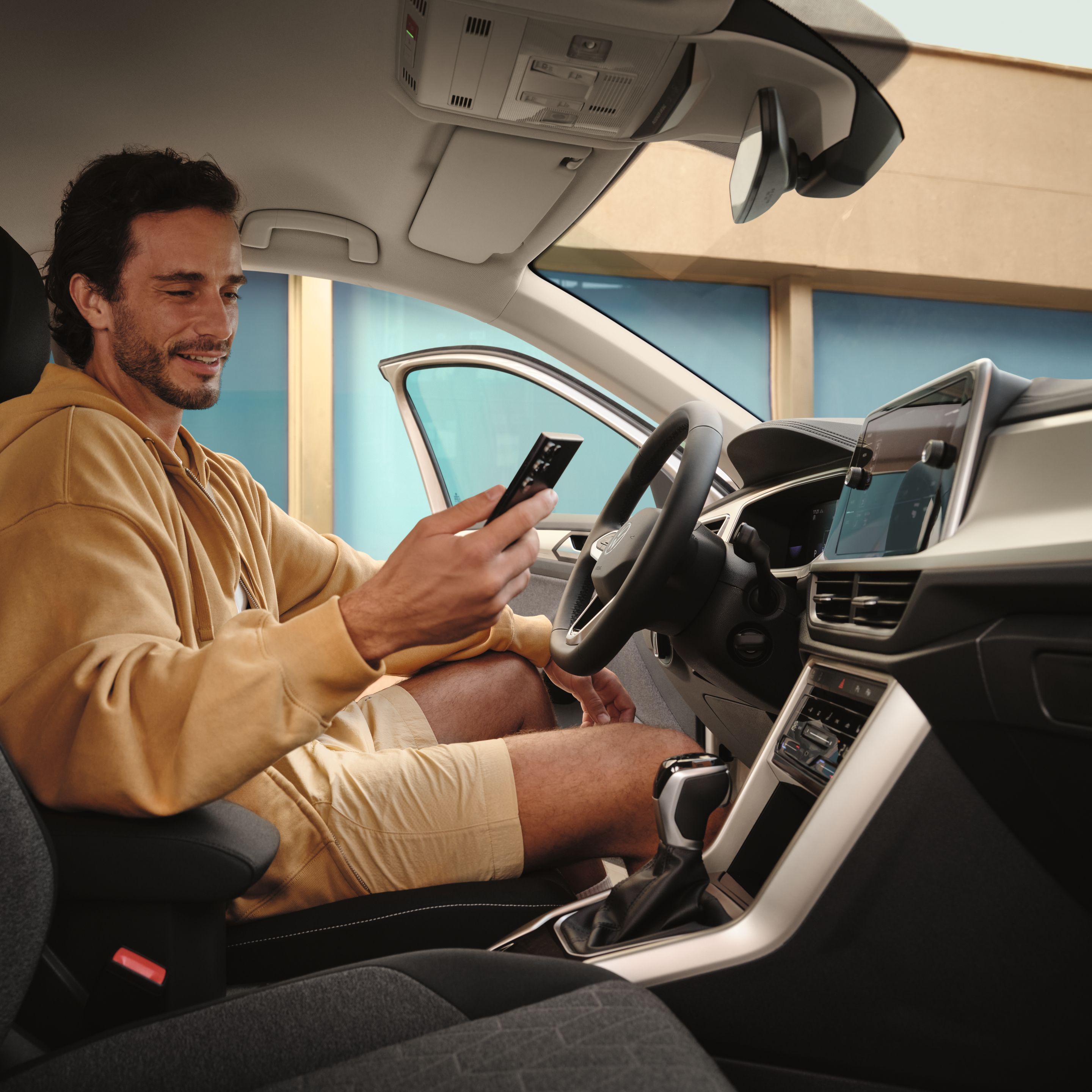 Mann sitzt in VW T-Roc und blickt auf Smartphone