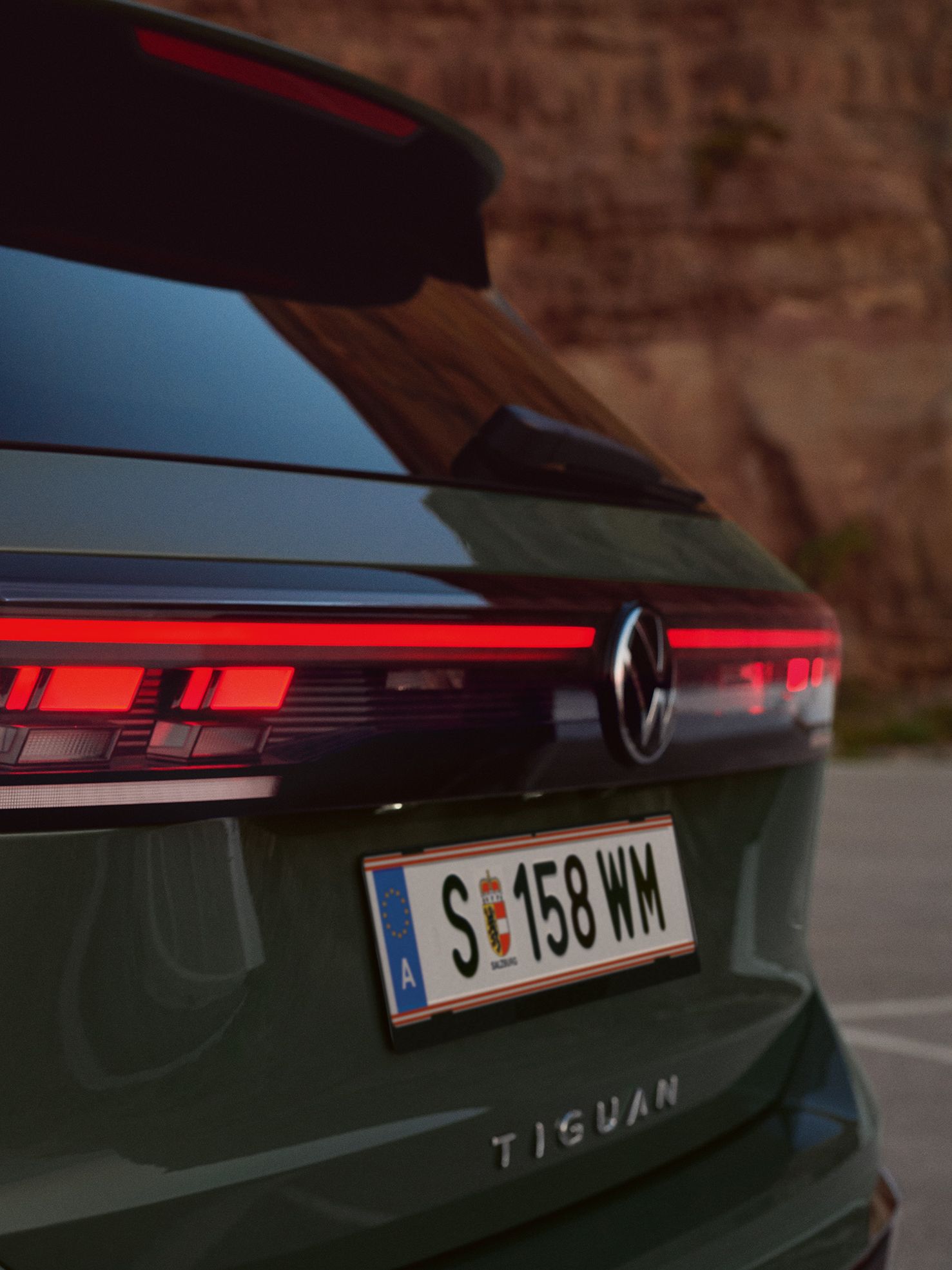 Detailansicht der Heck-Lichtsignatur eines vor einer felsigen Landschaft geparkten dunkelgrünen VW Tiguan.