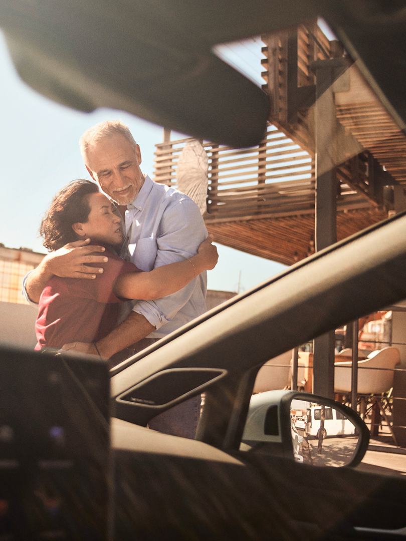 Blick durch die Windschutzscheibe eines VW Golf, ein Mann und eine Frau umarmen sich